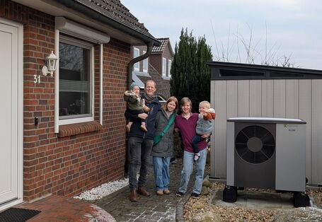 Familie vor einem Einfamilienhaus mit Wärmepumpe