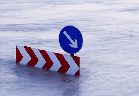 Ein Verkehsschild steht mitten im Hochwasser. Die Straße ist nicht mehr zu sehen.