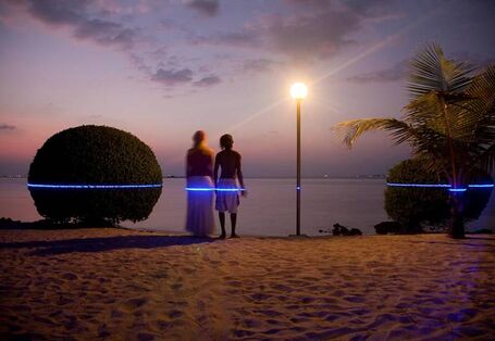 Ein Pärchen steht am Strand blickt in den Sonnenuntergang über dem Meer. In Hüfthöhe zeigt ein blauer Laser, wie hoch Ihnen das Wasser stehen könnte. 
