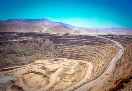Panoramaufnahme einer Kupfermine: Vorblauen Himmel sieht man die vielen abgetragenen Erdschichten, eine gigantische Kluft.