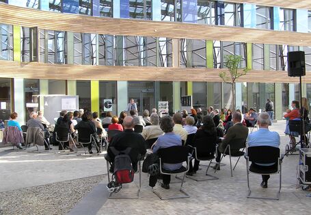 Das Publikum der Austellungseröffnung hört einem Redner zu