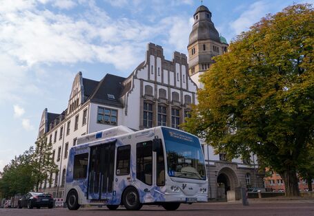 Ein mit Wasserstoff betriebener Kleinbus steht auf der Straße vor einem alten Gebäude und einem Baum