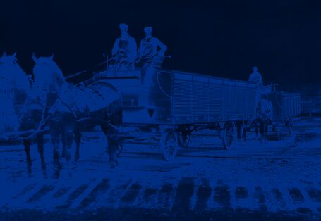 Pfedewagen mit zwei Arbeitern auf dem Kutschbock, die Ladefläche ist mit Metall-Rolläden abgedeckt. 