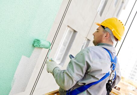 Arbeiter streicht Hausfassade grün an