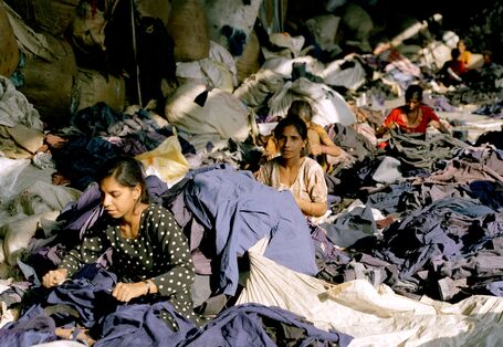 Frauen zerschneiden Jacken und Oberteile; die eingenähten Etiketten werden herausgeschnitten - Marken und Labelsangaben werden bei dem Prozess wertlos.