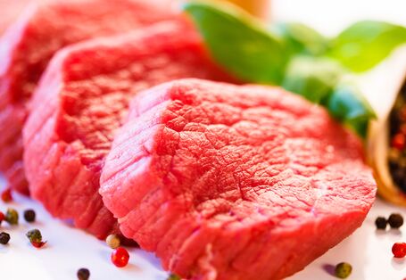 Drei Scheiben rohes Rindfleisch, umgeben von buntem Pfeffer und Deko