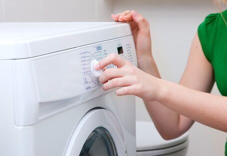 Eine Frau dreht am Programmwählknopf einer Waschmaschine.