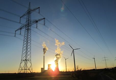 Übertragungsmasten mit Hochspannungsleitungen, Windräder und konventionelles Kraftwerk vor Sonnenuntergang.