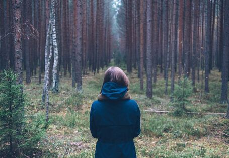 Frau steht mit Rücken zugewandt im Wald.
