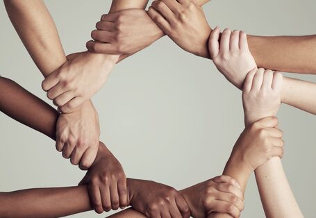 Hände von Personen mit verschiedenen Hautfarben halten sich aneinander fest und bilden einen Kreis.