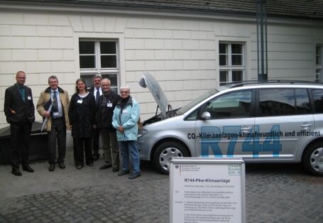 A group of persons standing beside a silver VW Touran with the inscription "R744"