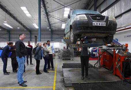 Ein Auto in einer Werkstatt auf einer Hebebühne, daneben stehen mehrere Personen