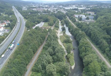 Ein renaturierter Fluss in der Mitte, links eine Autobahn, rechts Bahngleise.