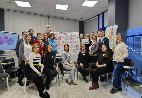 Eine Gruppe von Menschen sitzt bzw. steht vor einem Flipchart.