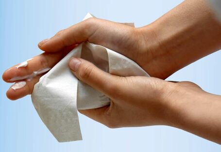 Photo showing hands with white cream, which is wiped off with a paper towel.
