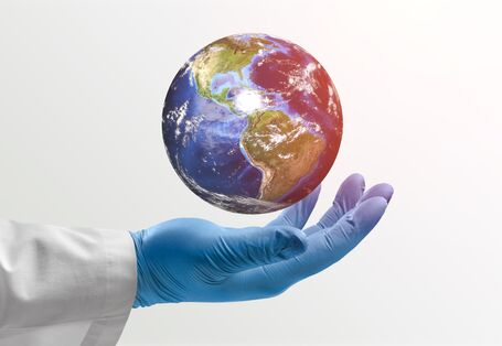 Photo of an arm with a doctor's coat and gloves holding a globe.