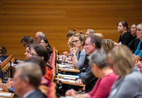 Sie sehen ein Bild welches auf der 1. Nationale Konferenz 2018: „Klimaanpassungsdienste – Klimavorsorge in der Praxis aufgenommen wurde. Sie sehen drei Reihen (von der Seite fotographiert) eines voll besetzten Hörsaals. Alle Menschen schauen sehr konzentriert und bis auf eine weibliche Person die gespannt nach vorne Blickt, sind alle Personen unscharf dargestellt.