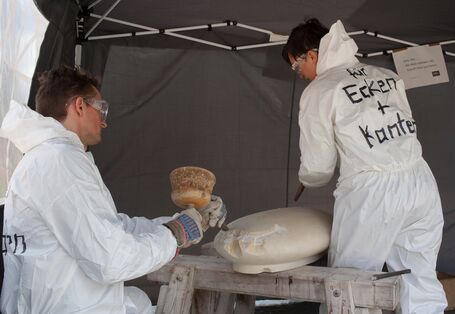 Zwei Menschen in Schutzanzügen bearbeiten Stein