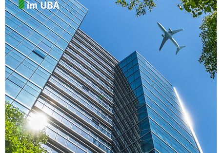 Flugzeug fliegt in blauem Himmel über ein verglastes Hochhaus.