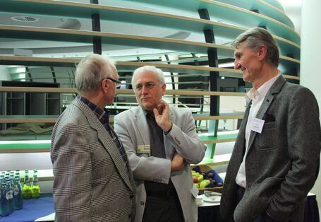 Drei  ältere Männer im Jacket stehen in einem Kreis zusammen und reden.