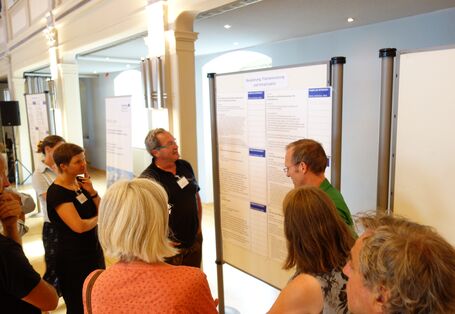 Einige Teilnehmende schauen sich eine Informationstafel an, die von einer Person vorgestellt wird.