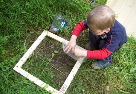 Ein Kind guckt sich den Boden innerhalb eines Holzrahmens ganz genau an und füllt eine Probe in eine Plastiktüte