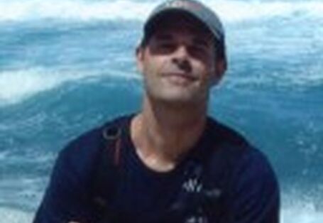 Ein Foto des Künstlers Sven Hoffmann lächelnd mit verschränkten Armen vor reißendem Wasser stehend.