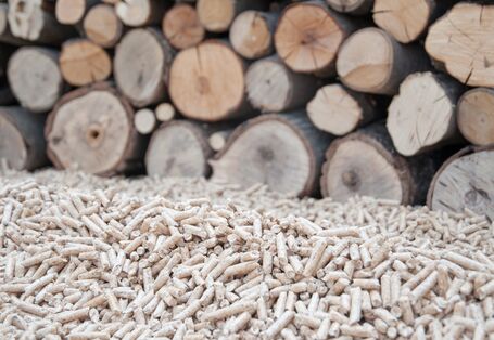 Holzpellets vor einem Holzstapel