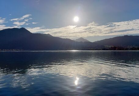 The picture shows a mountain lake in glaring sunlight. A mountain chain is visible in the background.