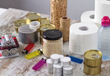 The picture shows an assortment of emergency provisions including groceries such as beans, rice and tinned food, batteries, adhesive tape, toilet paper, tea lights and lighters.