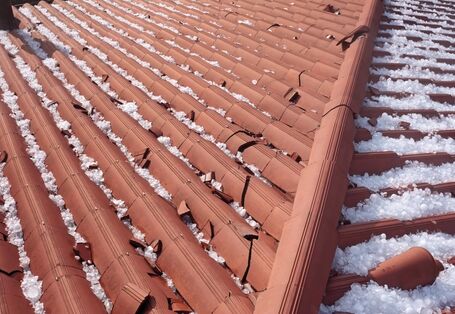 The picture shows the top view of a building roofed with red tiles. To the right and left of the roof ridge you can see numerous large hailstones. Some of the roof tiles are broken.