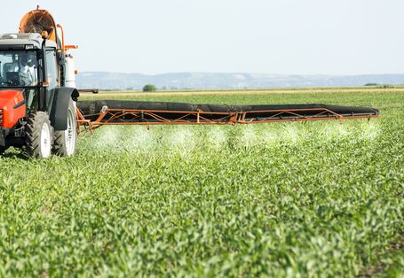 Ein Feld mit einem Pflanzenschutzgerät, welches Düngermittel verteilt 