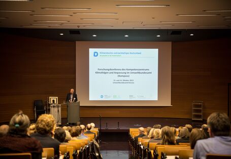 Ein Vortragender steht vor dem Hintergrund der Präsentation am Rednerpult