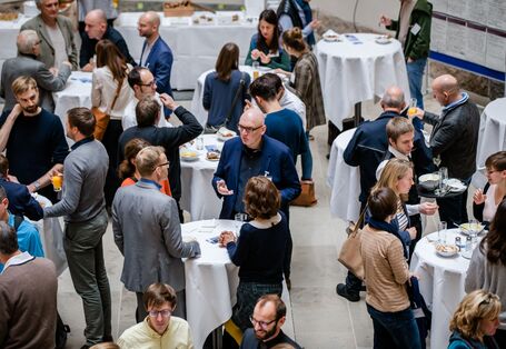 Der Blick geht von oben auf die Teilnehmenden, die alle an den Stehpulten stehen und Mittag essen. Alle unterhalten sich angeregt miteinander.