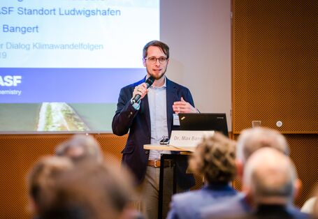 Vortragender steht mit Mikrofon in der Hand am Stehpult. Im Hintergrund ist seine Präsentation abgebildet.