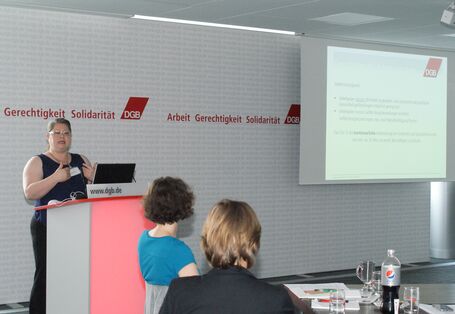 Vortragende steht am Rednerpult und trägt gestikulierend ihre Präsentation vor