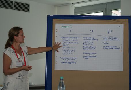 Teilnehmerin steht an der Moderationswand und zeigt auf die Ergebnisse der Arbeitsgruppe 3.