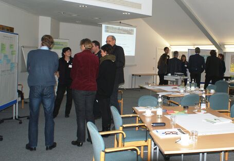 Teilnehmer stehen im Workshopraum in Grüppchen vor den Moderationswänden im Dialog miteinander.