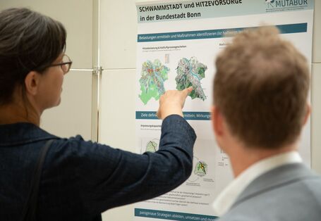 Auf dem Postermarktplatz im Forum des UBA zeigt ein Teilnehmender in dunkler Kleidung auf ein Poster. Ein anderer Teilnehmende in heller Kleidung schaut interessiert zu.