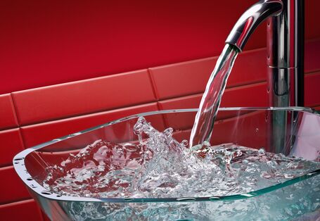 Laufender Küchenwasserhahn mit Glasschale, roter Hintergrund