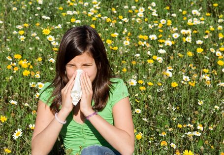A girl blows her nose. In the background is a flower meadow with daisies an dandelion.