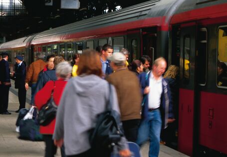 Zug im Bahnhof mit Menschengruppen am Gleis