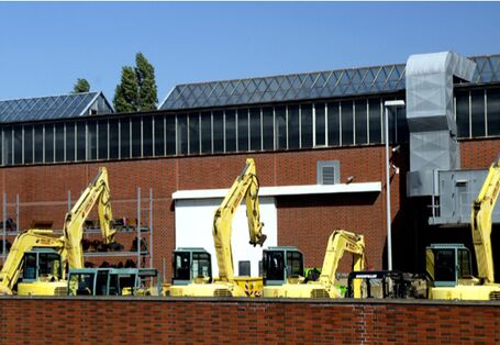 Fünf Bagger stehen auf einer Gewerbefläche vor einer Industriehalle