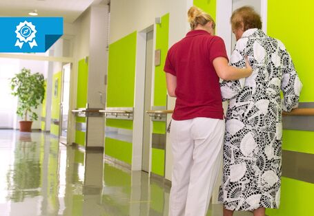 Eine Pflegekraft unterstützt eine Patientin beim Laufen.