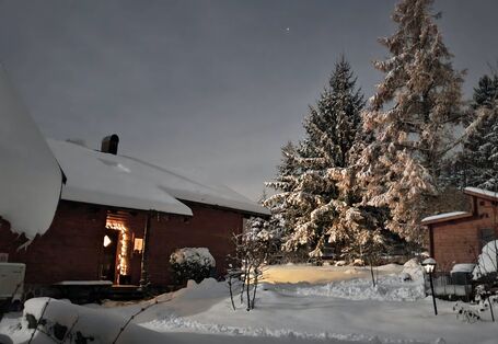 Eine Wärmepumpe vor Holzhaus im Schnee.