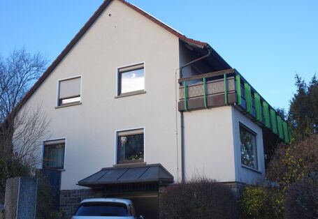 Das Gebäude von Südost mit dem Balkon über die gesamte Gebäudelänge, die Effizienz-Wärmepumpe steht unterhalb der linken Fenster