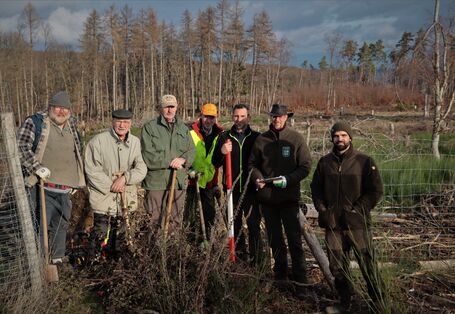Es stehen sieben Personen in einer Waldfläche. Vier personen halten einen Spaten.