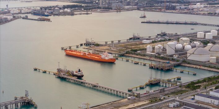Großer, roter Öltanker an einem Raffinerieterminal mit weißen Lagertanks, Pipelinenetzwerken und Offshore-Ladeplattformen