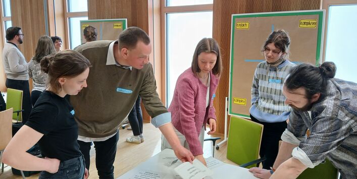 Fünf junge UBA-Wissenschaftler*innen stehen um einen Tisch herum und arbeiten gemeinsam an einer Aufgabe. 