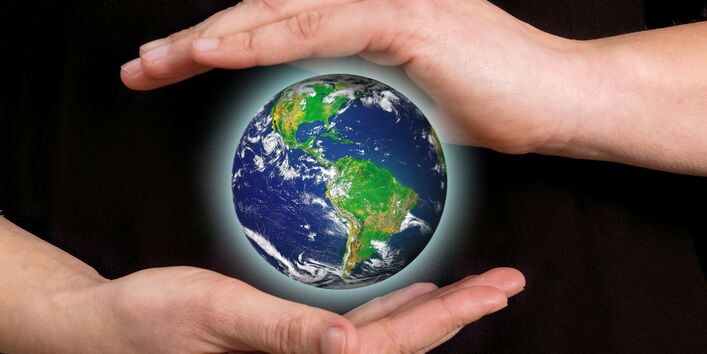 ein Mensch hält seine Hände schützend um den Planeten Erde